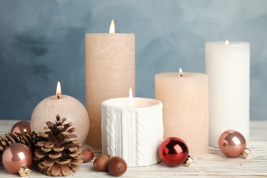 Composition with burning candles and Christmas decoration on white wooden table against blue background