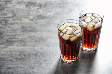 Photo of Glasses of cold cola on grey table. Space for text