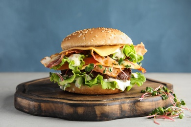 Photo of Tasty burger with bacon on table against color background
