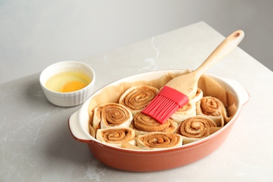 Photo of Baking dish with raw cinnamon rolls and pastry brush on table