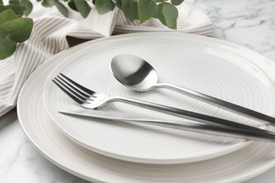 Photo of Stylish setting with cutlery, napkin, eucalyptus branches and plates on white marble table, closeup