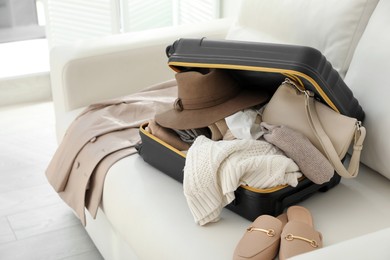 Photo of Open suitcase full of clothes, jacket and fashionable shoes on sofa in room