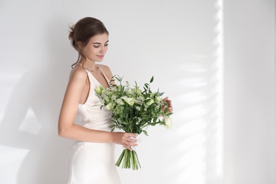 Photo of Young bride wearing wedding dress with beautiful bouquet on light background