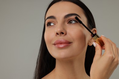 Photo of Beautiful young woman applying mascara on grey background, closeup