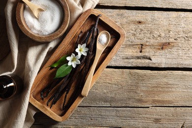 Photo of Vanilla pods, flowers, leaves and sugar on wooden table, top view. Space for text