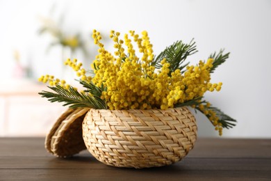 Photo of Beautiful mimosa flowers in wicker basket on wooden table indoors