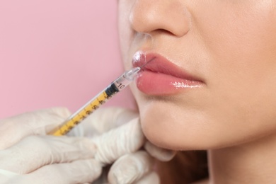 Photo of Young woman getting lips injection on color background, closeup. Cosmetic surgery