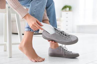 Photo of Woman putting orthopedic insole into shoe at home, closeup