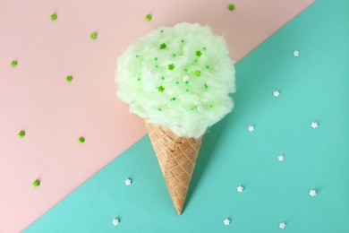 Photo of Sweet cotton candy in waffle cone on color background, top view