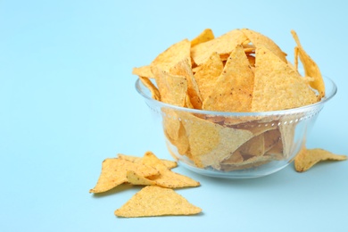 Photo of Glass bowl of tasty Mexican nachos chips on light blue background