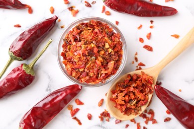 Photo of Chili pepper flakes and pods on white marble table, flat lay
