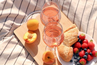 Photo of Glasses of delicious rose wine and food on white picnic blanket