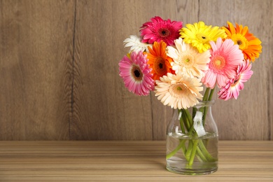 Photo of Bouquet of beautiful bright gerbera flowers in glass vase on table against wooden background. Space for text