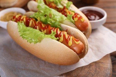 Photo of Tasty hot dogs with lettuce, ketchup and mustard on board, closeup