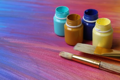 Photo of Jars with paints and brushes on abstract picture, closeup. Space for text