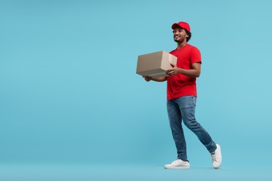 Happy young courier with parcel on light blue background, space for text