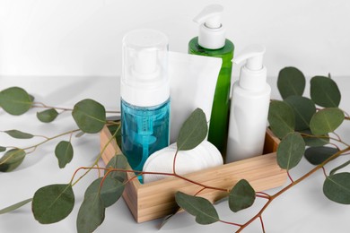 Different face cleansing products, cotton pads and eucalyptus leaves on white table