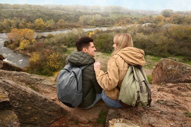 Photo of Couple of hikers with travel backpacks enjoying beautiful view near mountain river