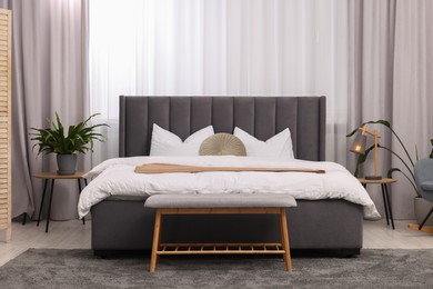Photo of Stylish bedroom interior with large bed, ottoman, lamp and houseplants