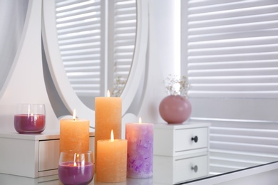 Photo of Different burning candles on dressing table in room