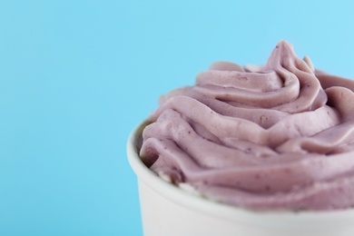 Photo of Cup with tasty frozen yogurt on light blue background, closeup. Space for text