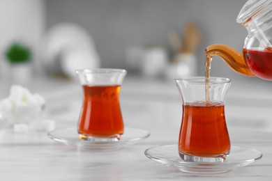 Photo of Pouring traditional Turkish tea from pot into glass on white table, space for text