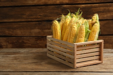 Photo of Crate of sweet corn cobs on wooden table. Space for text