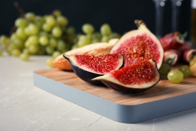 Wooden board with ripe fig slices on grey table, closeup