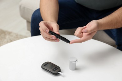Photo of Diabetes test. Man checking blood sugar level with lancet pen at white table, closeup