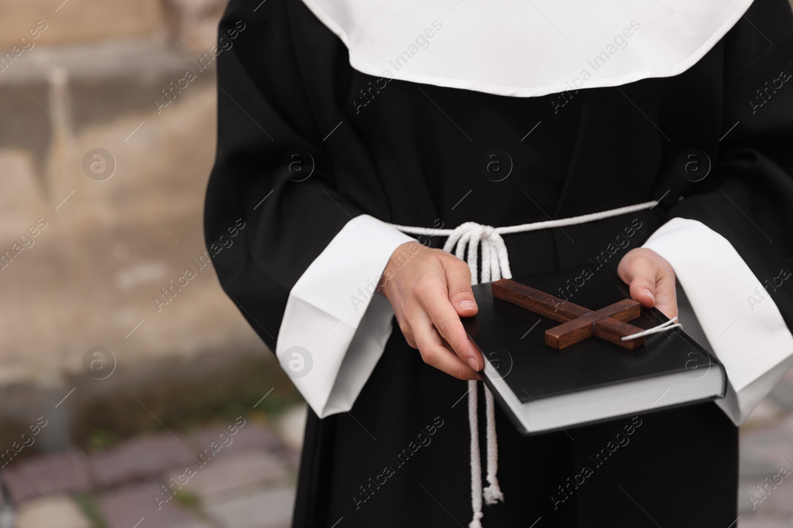 Photo of Young nun with Christian cross and Bible outdoors, closeup