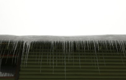 Photo of House with icicles on roof, low angle view. Winter season