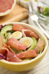 Photo of Delicious pomelo salad with prosciutto in half of fruit on white wooden table, closeup