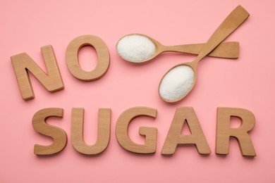 Photo of Words No Sugar made of wooden letters and spoons on pink background, flat lay