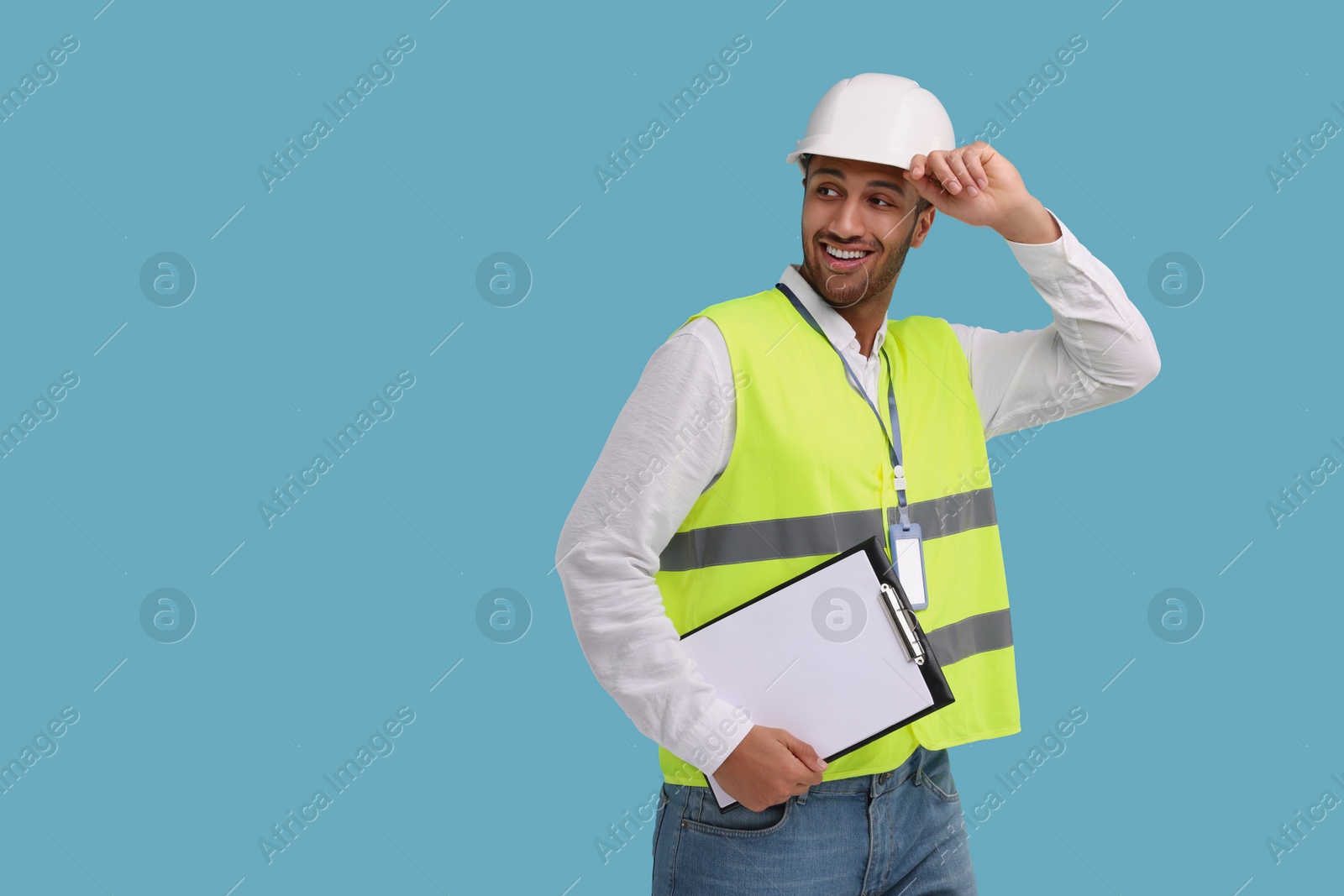 Photo of Engineer in hard hat holding clipboard on light blue background, space for text