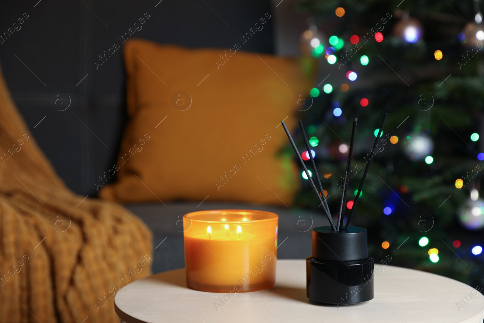 Photo of Aromatic reed air freshener and candle on white wooden side table in cozy room