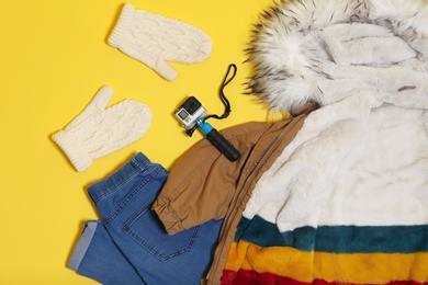 Photo of Set of warm clothes and action camera on color background, flat lay. Winter vacation