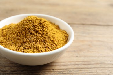 Photo of Dry curry powder in bowl on wooden table, closeup. Space for text