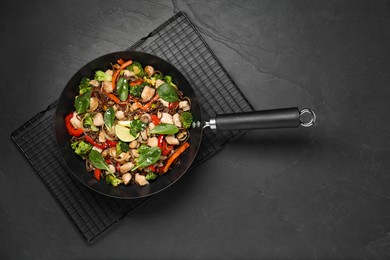 Photo of Stir-fry. Tasty noodles with meat and vegetables in wok on grey textured table, top view
