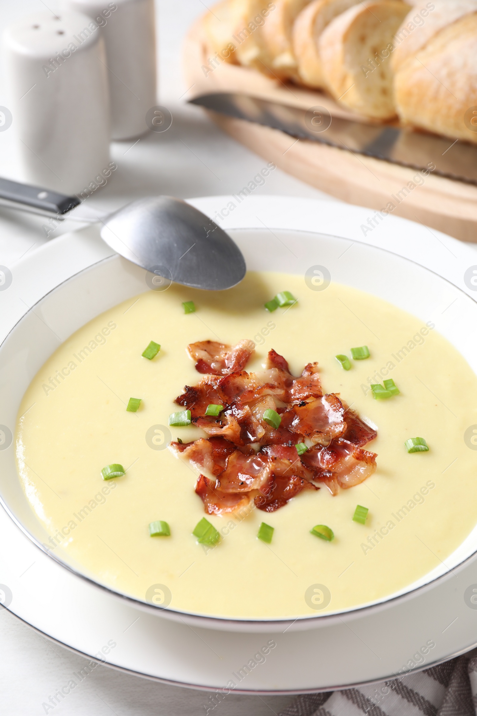 Photo of Tasty potato soup with bacon in bowl and spoon on white table, closeup