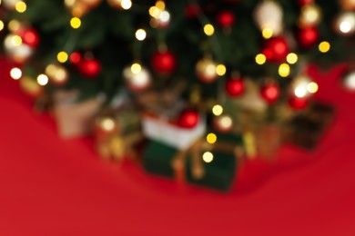 Photo of Blurred view of beautifully decorated Christmas tree on red background, closeup