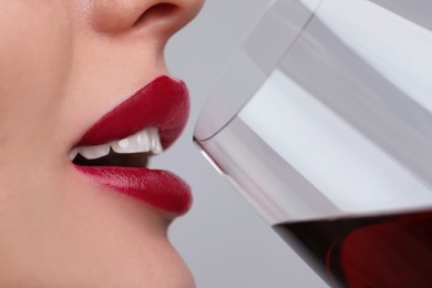 Photo of Closeup view of beautiful young woman with perfect lips makeup drinking wine on light grey background