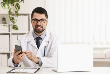 Photo of Male doctor with smartphone at table in office