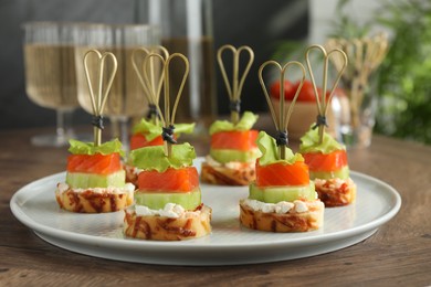 Photo of Tasty canapes with salmon, cucumber, bread and cream cheese on wooden table, closeup
