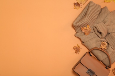 Photo of Flat lay composition with sweater and dry leaves on orange background, space for text. Autumn season