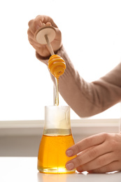 Photo of Woman with honey and dipper at white table, closeup