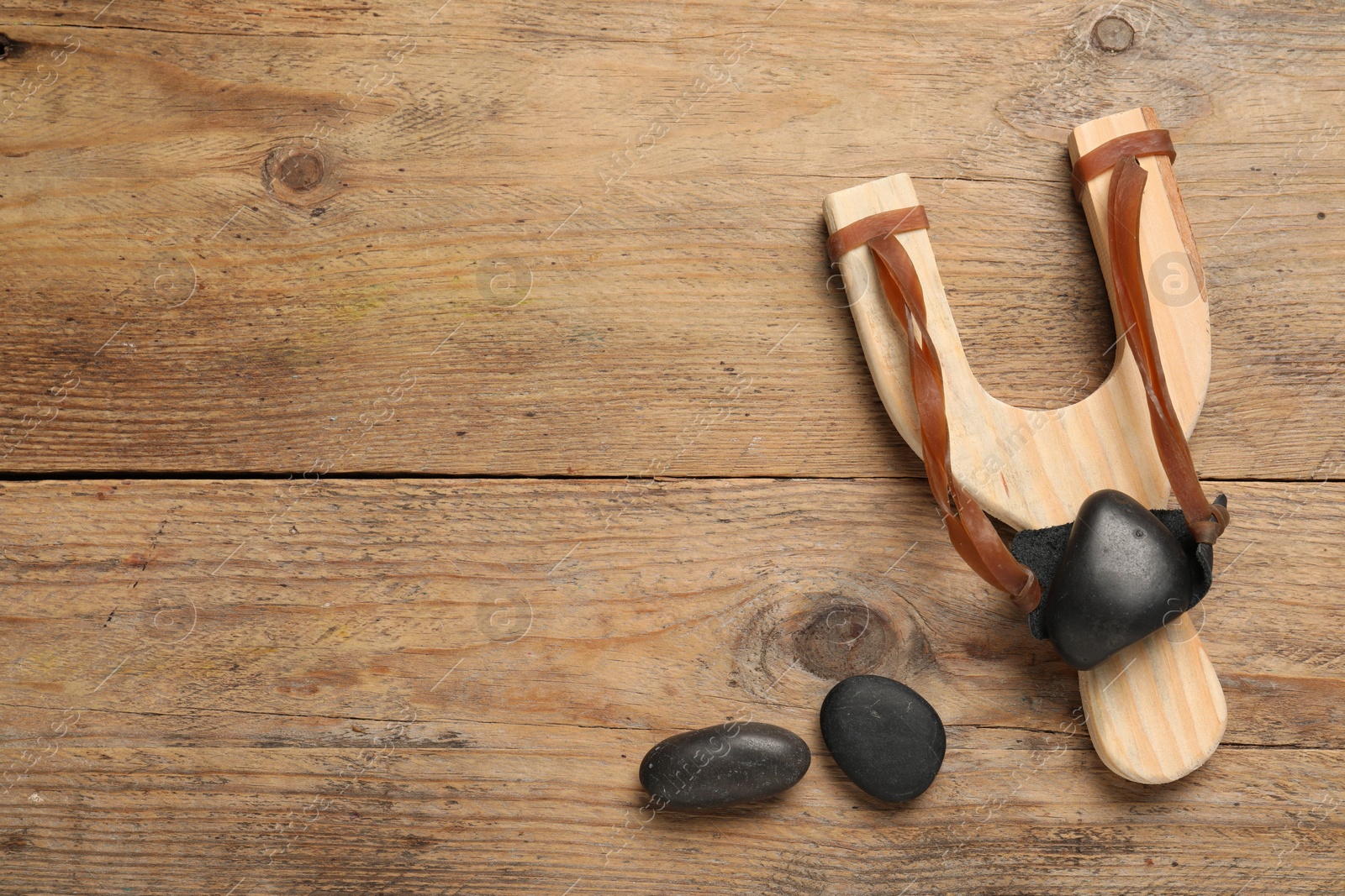 Photo of Slingshot with stones on wooden background, flat lay. Space for text