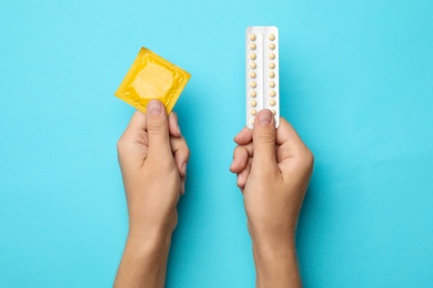 Photo of Woman holding condom and birth control pills on blue background, top view. Safe sex