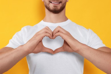 Photo of Happy volunteer making heart with his hands on orange background, closeup