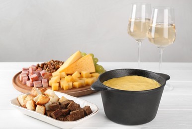 Photo of Fondue with tasty melted cheese, different products and aromatic wine in glasses on white wooden table