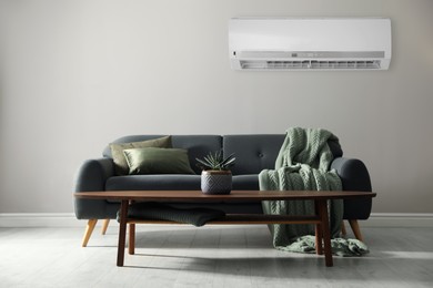 Image of Modern air conditioner on light grey wall in room with stylish sofa